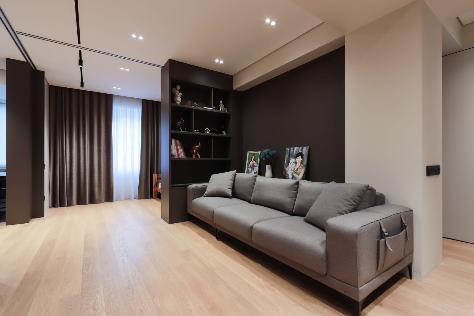 Living room with grey sofa, dark shelving and oak flooring